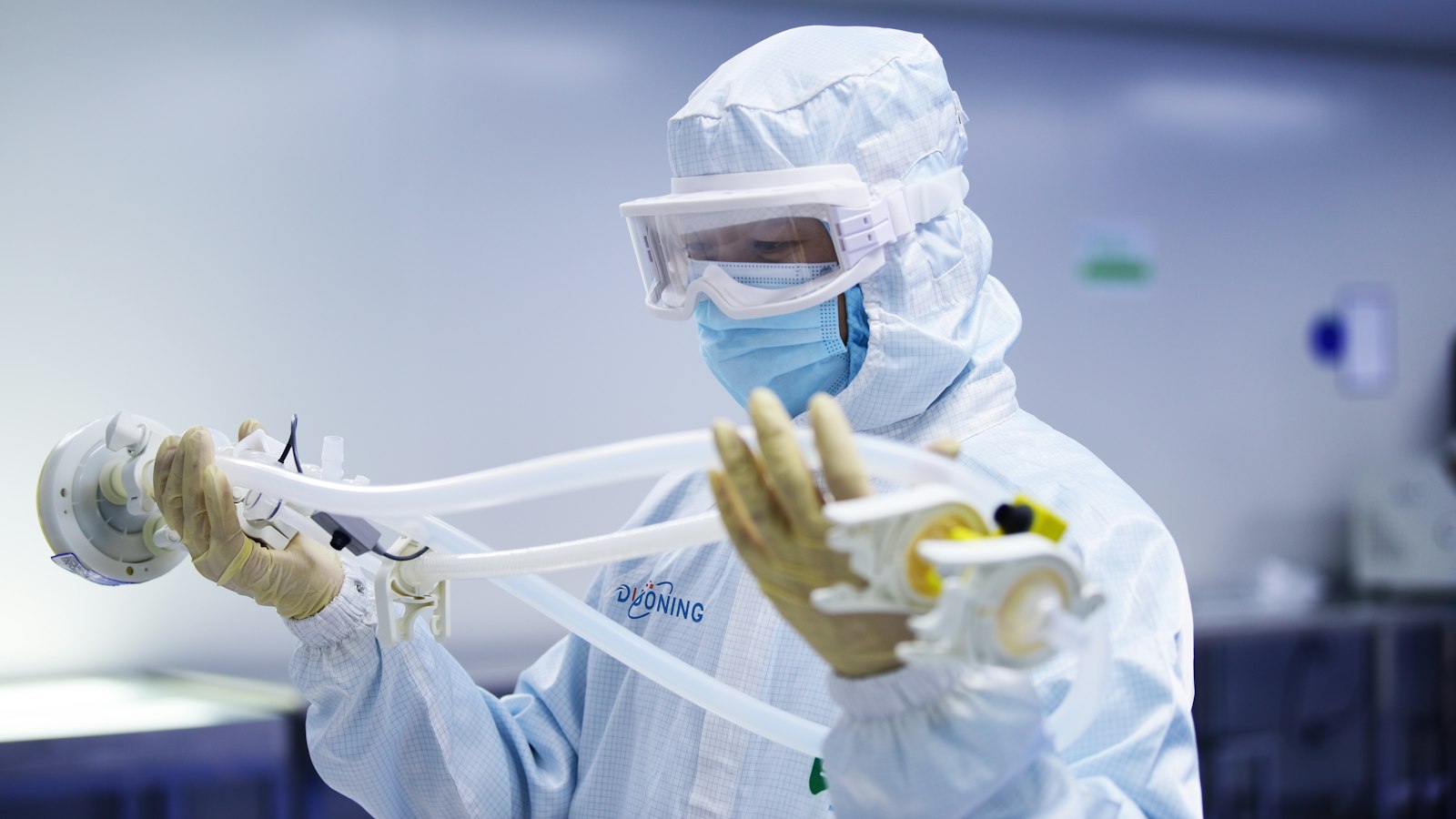 An operator in a cleanroom suit and goggles handling single-use tubing